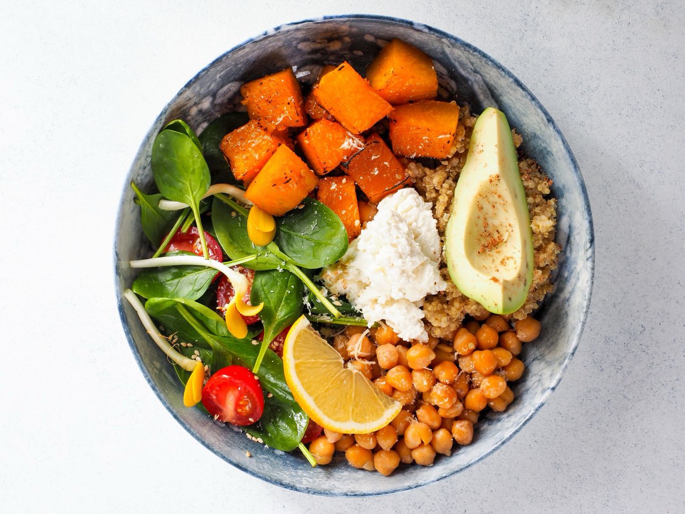 A balanced salad bowl with leaves, roasted squash, chickpeas, avocado and a lemon slice